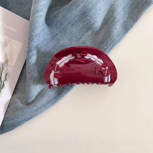 Close-up of burgundy cherry claw clip with white wavy edges on denim and table surface