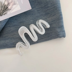 Detail view of large wavy cream white hair claw clip on dark blue denim fabric background