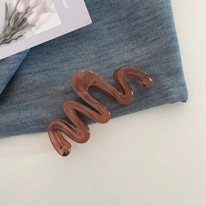 Close-up of a large brown wave-shaped hair claw clip on denim and white background