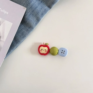 Vue détaillée de la pince à cheveux pomme avec boutons colorés sur fond minimaliste