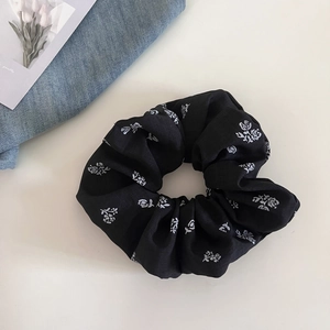 Detail shot of a black floral scrunchie with white rose print on a soft cream surface