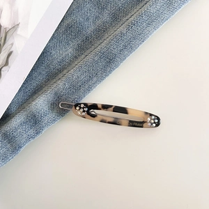 Detail of tortoise shell acetate hair clip with rhinestones and gold lettering on denim