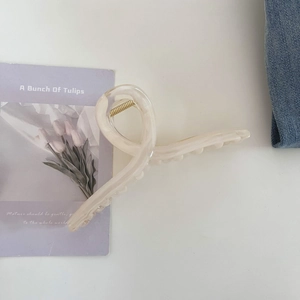 Détail d'une grande pince à cheveux marbrée crème avec ressort doré sur fond blanc