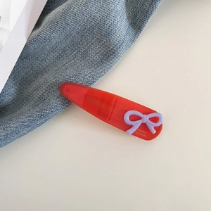Détail d'une pince à cheveux en acétate rouge avec nœud mauve et texte doré
