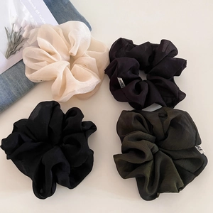 Detailed macro view of four textured tulle scrunchies in cream, black, green and grey colors