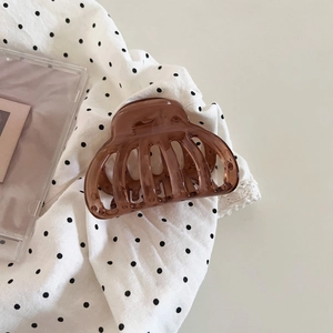 Minimalist brown translucent hair claw clip with sleek curved design on vintage polka dot fabric