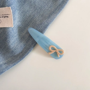 Détail d'une pince à cheveux goutte en acétate bleu ciel avec nœud beige et étiquette dorée
