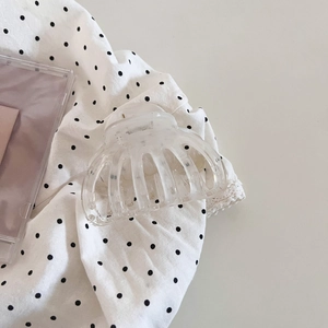 Detail of a clear minimalist acrylic hair claw clip on a polka dot fabric background