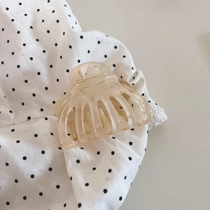 Detail of peach translucent hair claw clip with golden metal spring on polka dot fabric