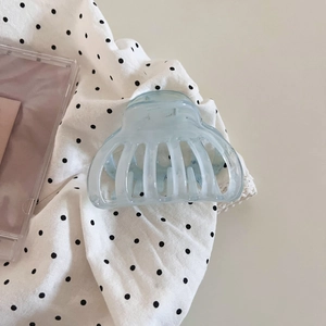 Detail view of a pale blue translucent shark hair clip on a polka dot fabric background