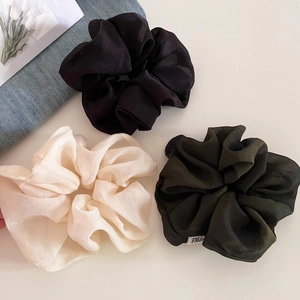 Three premium textured tulle scrunchies in black, cream, and dark green with label detail