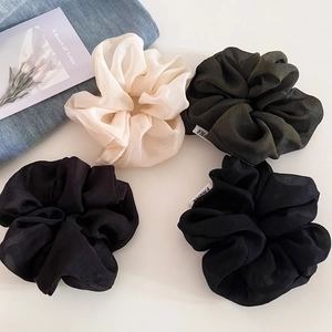 Detailed view of four textured tulle scrunchies in cream, olive green, and black