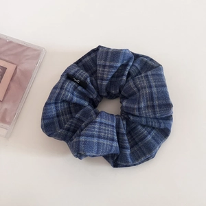 Detailed view of dark blue plaid scrunchie with thick fabric texture and side logo tag