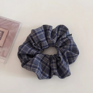 Detail view of navy plaid fabric scrunchie with brand logo on a minimalist background