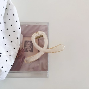 Détail macro d'une pince à cheveux crème translucide avec design croisé et ressort