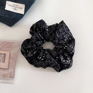 Detailed close-up of a black paisley scrunchie with vintage patterns on a white background
