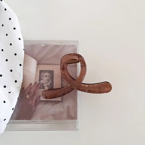 Détail de la pince à cheveux marron foncé avec ressort doré sur fond minimaliste