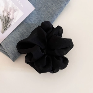Close-up of black pleated sheer fabric scrunchie with textured chiffon finish for hair