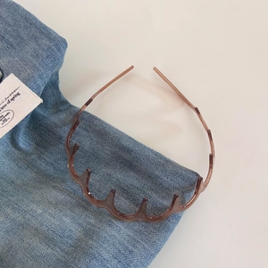 Close-up of wavy amber resin headband with non-slip teeth on a denim background