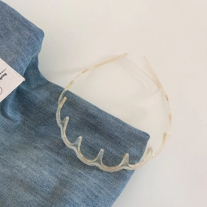 Macro detail of wave-shaped clear resin headband with non-slip teeth on denim fabric