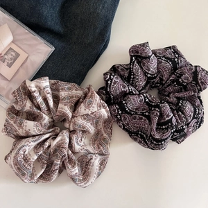 Detailed view of large paisley print silk scrunchies in cream and black on denim