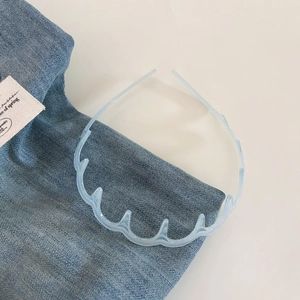 Detail of light blue wavy headband with non-slip teeth on blue denim fabric background