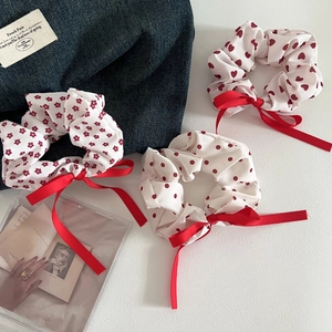 Close-up of three white scrunchies with red heart, floral, and polka dot patterns and bows