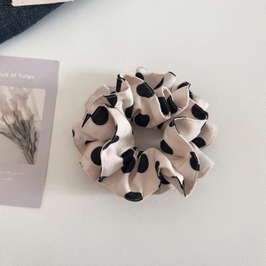 Detail of cream fabric scrunchie with large black polka dots on textured background