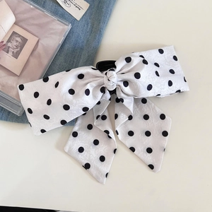 Elegant white polka dot ribbon bow hair clip on a stylish desk with aesthetic background