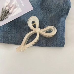 Detail of a creamy resin hair claw clip with a bow design on denim background