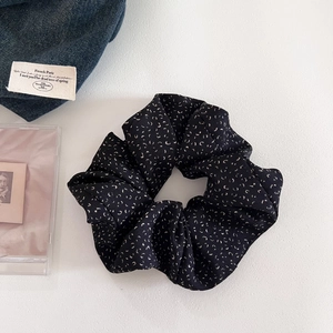 Close-up of black scrunchie with white patterns on denim and white background