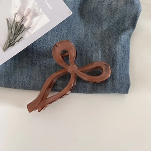 Detailed view of a glossy brown bow hair claw clip placed on blue denim jeans