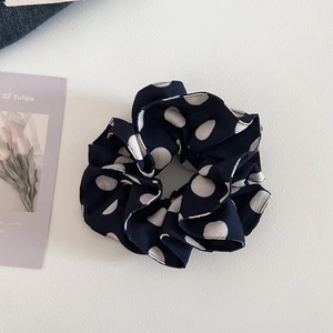 Macro shot of vintage navy blue scrunchie with white polka dots on a minimalist white surface