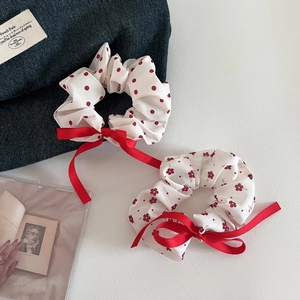 Detail view of two floral and polka dot hair scrunchies with red bows on blue denim