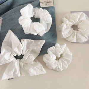 Détail de quatre chouchous blancs avec dentelle, broderie et nœud sur du denim