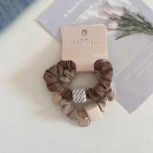 Detail view of coffee and beige satin hair scrunchies with gold tags on pink card