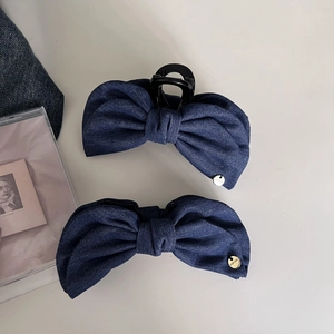 Detailed macro view of dark blue denim bow hair clips with gold logo pendant