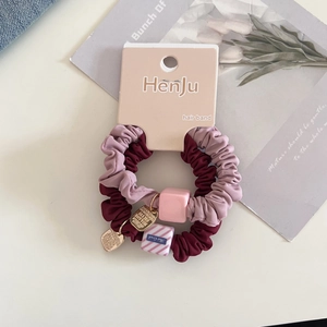 Close-up of set of 2 satin scrunchies in burgundy and pink with decorative gold heart charm