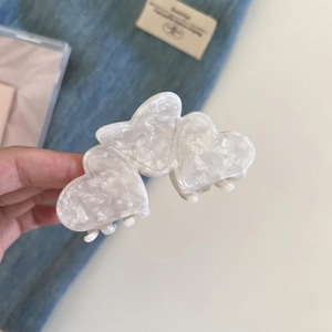 Close-up of marble white heart-shaped acetate claw clip held by hand for hair styling