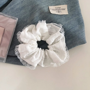 Détail d'un chouchou en dentelle blanche avec broderie fine sur fond de jean bleu