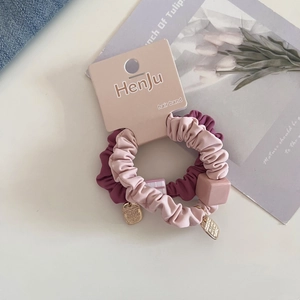 Detail of pink and purple pleated hair scrunchies with square charm and gold label