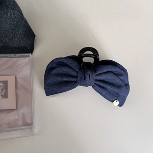 Retro dark blue denim bow banana hair clip with a gold metallic logo on white surface