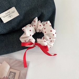 Detail view of a white polka dot scrunchie with a large red bow on denim fabric