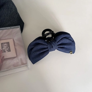 Detail of dark blue denim bow hair clip with gold metal tag on high-quality plastic claw