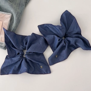 Detailed view of denim bow scrunchies with red stitching and golden charms for hair