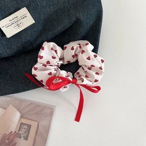 Detailed view of white scrunchie with red hearts and a long ribbon bow on denim