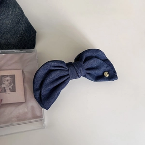Close-up of a dark blue denim bow hair clip with vintage golden metal buckle detail