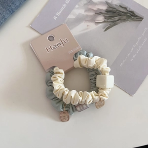 Close-up of dual-tone scrunchie with square bead and gold charm on brand paper card
