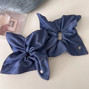 Detail view of denim fabric hair scrunchies with red stitching and metal logo tags