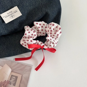 Close-up of a white floral scrunchie with a large red ribbon bow on a stylish background